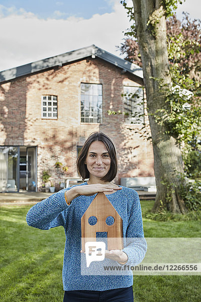 Portrait of smiling woman in garden of her home holding house model
