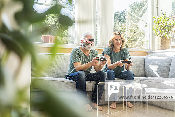 Glückliches reifes Paar  das zu Hause auf der Couch sitzt und Videospiele spielt.