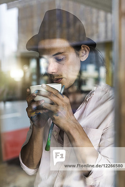 Künstler nimmt eine Pause von seiner Arbeit  lehnt sich gegen das Fenster  trinkt Kaffee