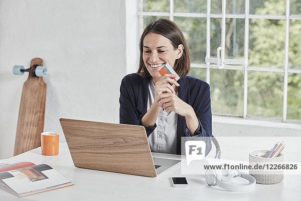 Happy businesswoman using laptop on desk holding card