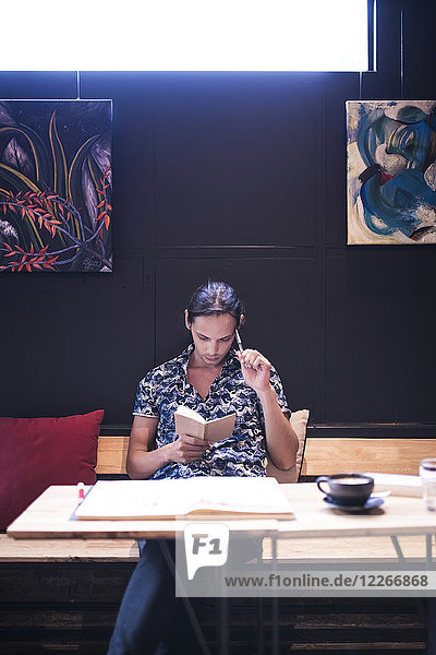 Künstlerin sitzt im Café und liest im kleinen Notizbuch