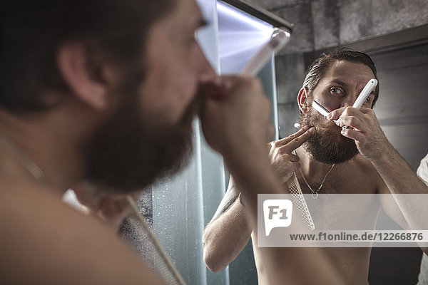 Portrait of bearded man looking at his mirror image while shaving