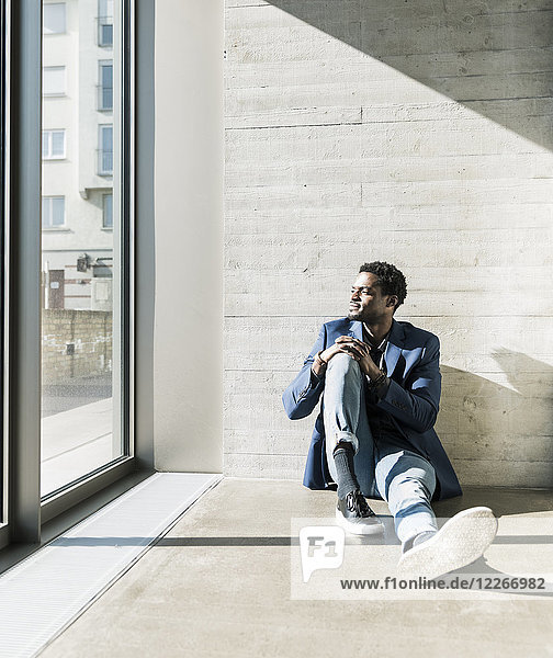 Businessman sitting on the floor in sunshine looking out of window