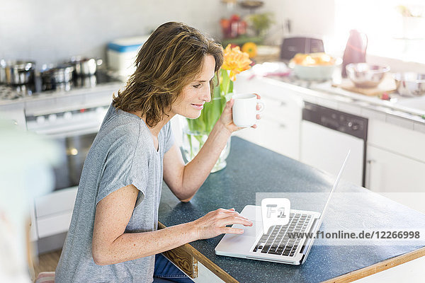Lächelnde Frau mit Laptop in der Küche zu Hause