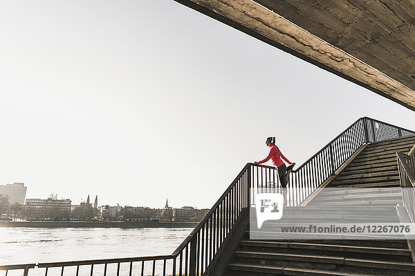 Junge Frau  die sich auf einer Treppe an einem Fluss in der Stadt ausstreckt