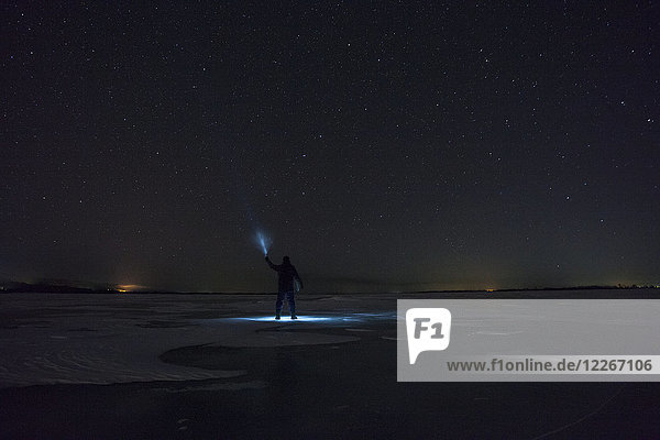 Russland  Oblast Amur  Silhouette des Menschen mit blauem Strahl auf dem gefrorenen Fluss Zeya bei Nacht unter dem Sternenhimmel.