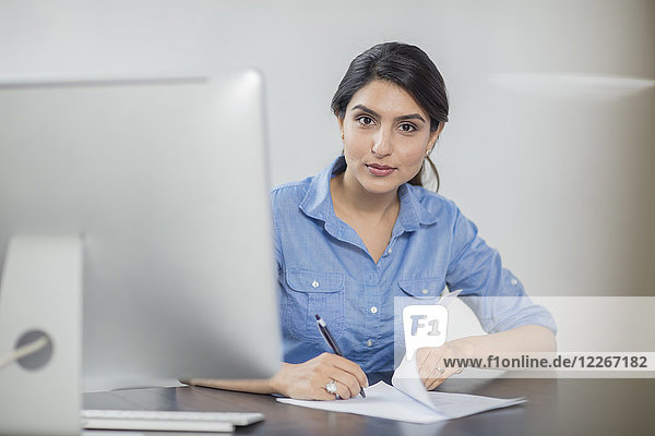 Porträt einer Geschäftsfrau beim Notieren am Schreibtisch im Büro