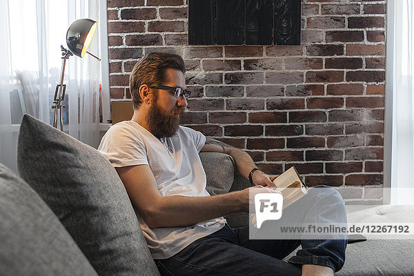 Man sitting on couch at home reading a book