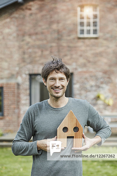 Porträt eines lächelnden Mannes vor seinem Haushaltenden Hausmodell