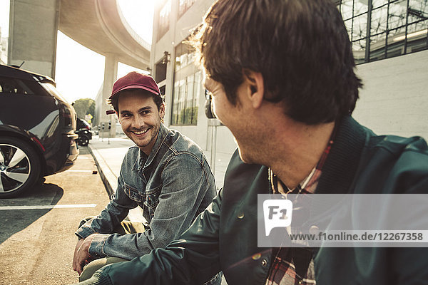Two smiling young men sitting on sidewalk