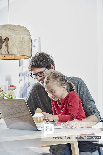 Lächelnder Vater und Tochter mit Laptop auf dem Tisch zu Hause