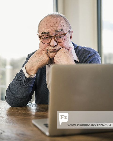 Senior man sitting at table looking at laptop