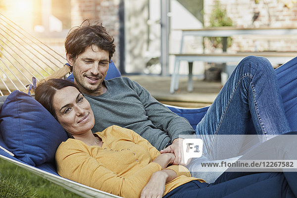 Smiling couple lying in hammock in garden of their home