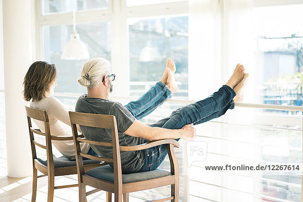 Entspanntes reifes Paar  das zu Hause auf Stühlen sitzt und die Füße hochlegt