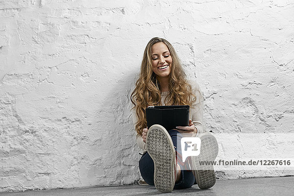 Portrait laughing young woman sitting on the floor using tablet