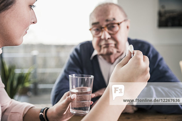 Frau hält Pille und Glas Wasser für älteren Mann