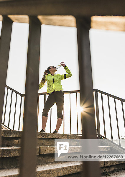 Sportliche junge Frau  die auf einer Treppe steht und aus der Flasche trinkt.