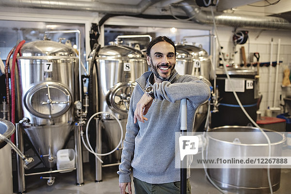 Portrait of mature manager standing against storage tanks at brewery