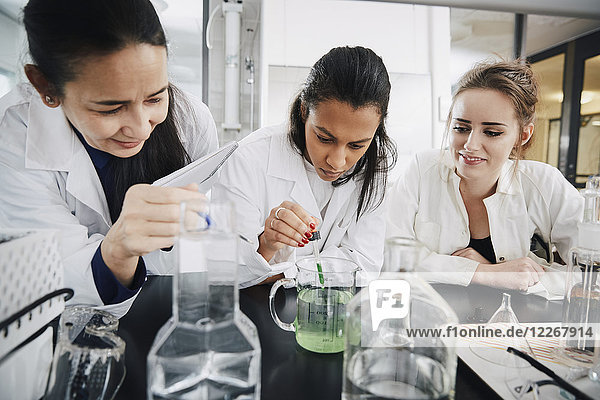 Reife Chemielehrerin betrachtet junge Studentin beim Mischen flüssiger Lösung im Becherglas