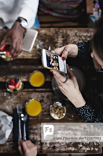 Hochwinkelansicht der Frau beim Fotografieren von Lebensmitteln über ein Smartphone am Tisch