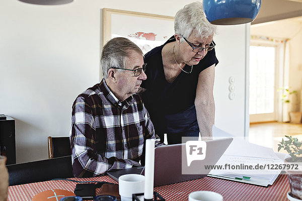 Senior couple with laptop at and financial bills at dining table