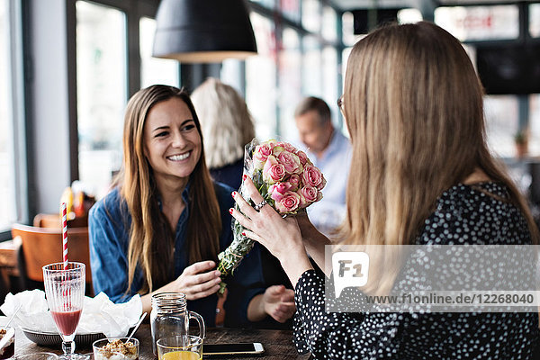 Lächelnde junge Frau schenkt der Freundin im Restaurant frischen Blumenstrauß