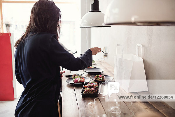 Frau beim Zubereiten des Essens auf dem Teller bei Tisch in der Werkstatt