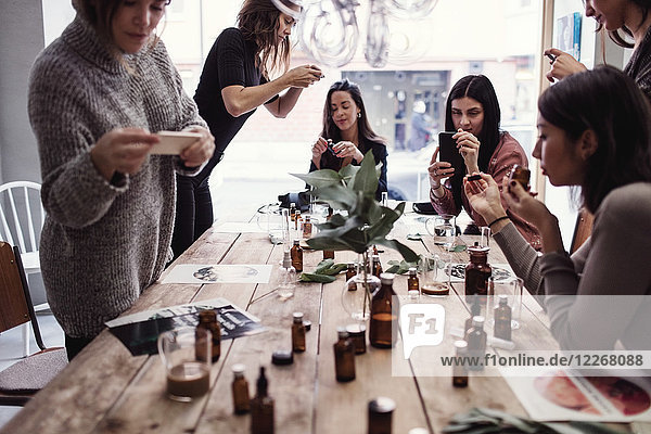 Multiethnische Mitarbeiterinnen beim Fotografieren von Parfums auf dem Tisch in der Werkstatt