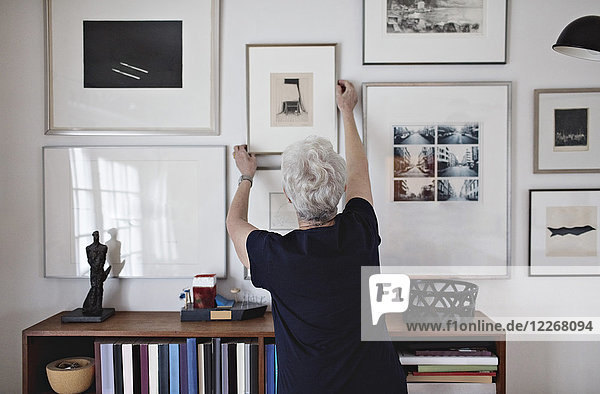 Rückansicht der pensionierten Seniorin mit Bilderrahmen an der Wand über dem Bücherregal zu Hause