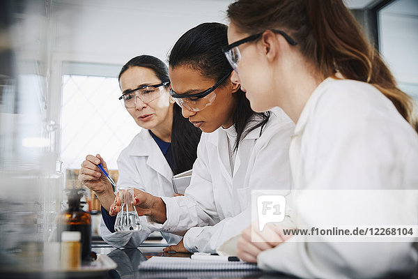 Female chemistry teacher explaining to young multi-ethnic students in laboratory