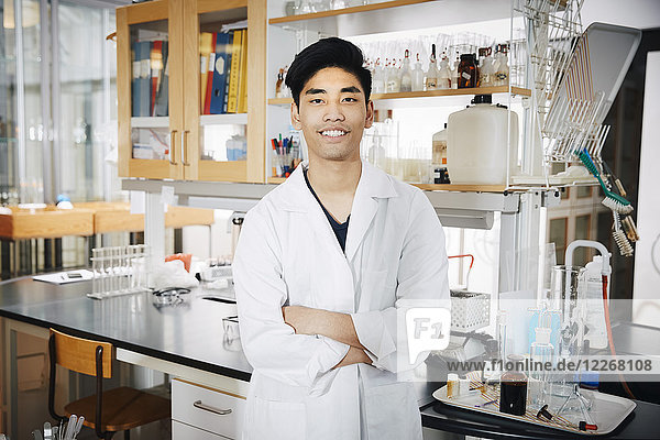 Portrait of confident young male university student standing with arms crossed at chemistry laboratory