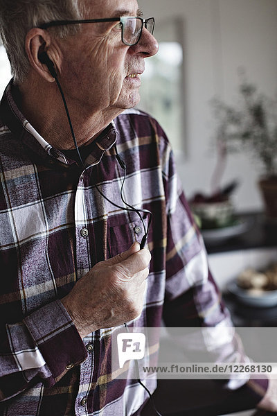 Senior Mann schaut weg  während er über In-Ear-Kopfhörer in der Küche zu Hause spricht.