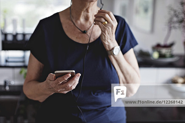Mittelteil der älteren Frau mit Smartphone in der Küche zu Hause
