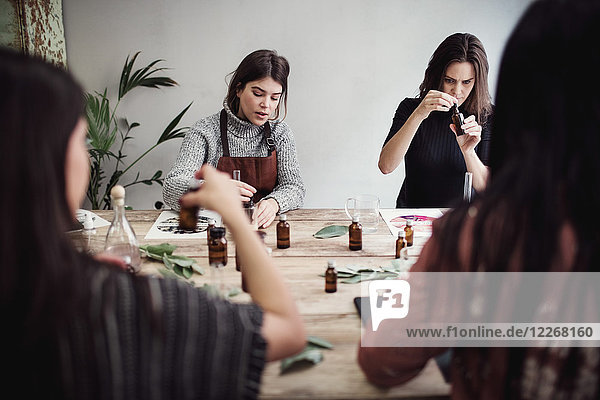 Multi-ethnic female colleagues preparing perfume while sitting at table in workshop