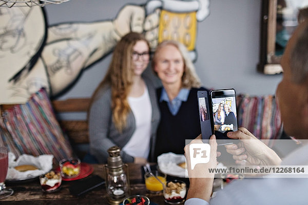 Reifer Mann fotografiert Frauen über Smartphone im Restaurant