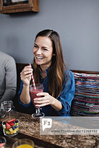 Smiling young woman having drink while sitting at table in restaurant