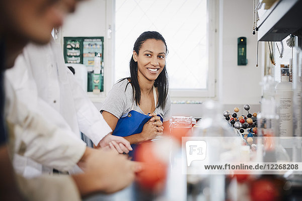 Selbstbewusste Studentin schaut sich Freunde an  die im Chemielabor sitzen