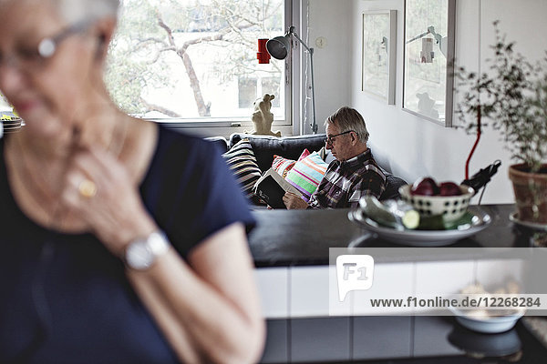 Seniorin in der Küche gegen Mann  der zu Hause auf dem Sofa sitzt