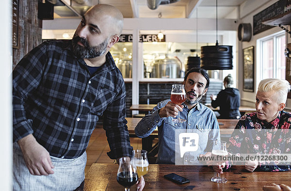 Customers examining various craft beer by bartender at bar