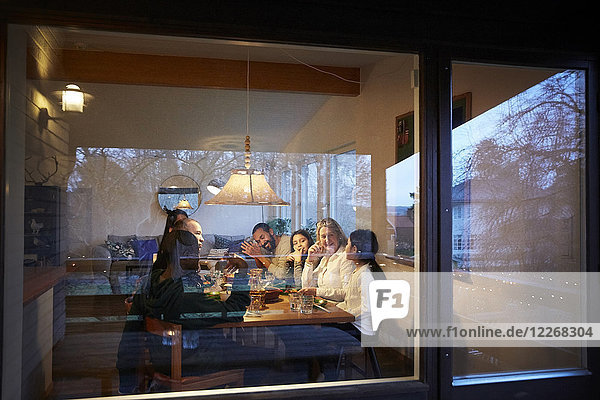 Glückliche Familie beim Abendessen am Tisch durch das Glasfenster bei Sonnenuntergang gesehen