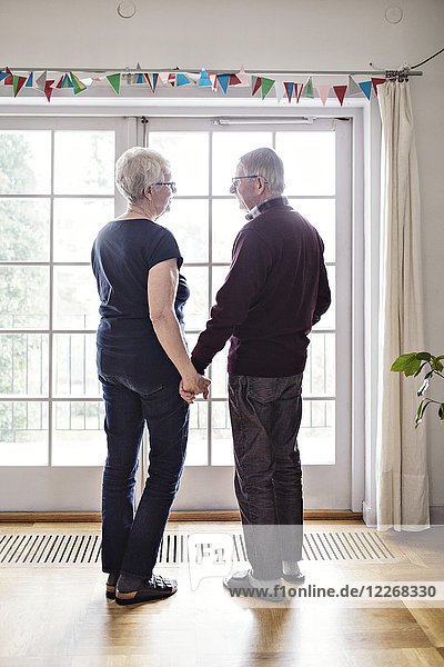 Volle Länge des pensionierten Paares  das zu Hause am Fenster steht.