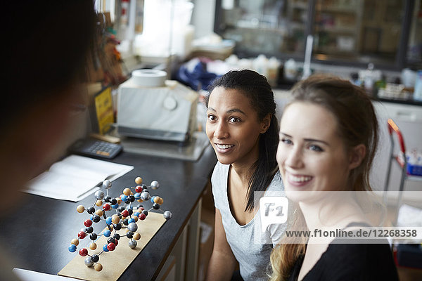 Lächelnde junge Studentinnen durch molekulare Struktur mit Blick auf die reife Lehrerin im Chemieunterricht