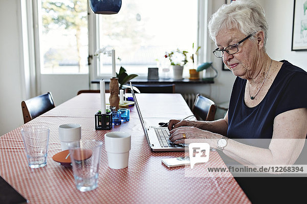 Senior woman using laptop while sitting at dining table in room