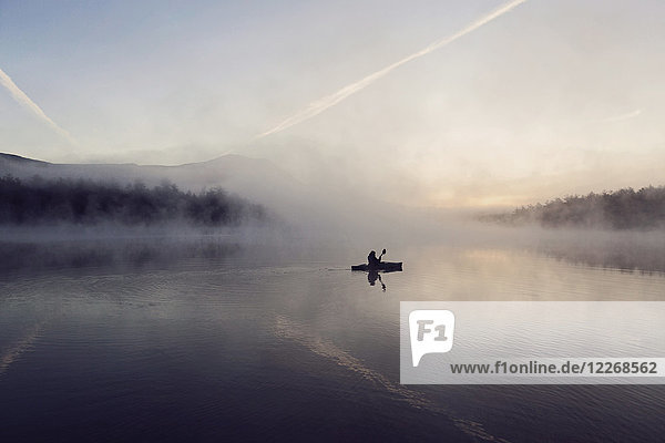 Young woman enjoys early morning paddle in kayak through mist on Daicey Pond in Maine's Baxter State Park  USA