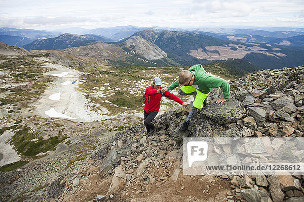 Father helping son down climb steep section of trail during hiking trip  Merritt  British Columbia  Canada