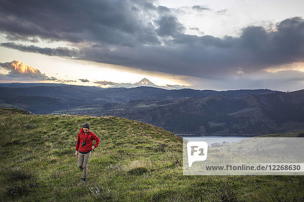 Large clouds over male hiker walking near edge of grassy cliff  Lyle  Oregon  USA