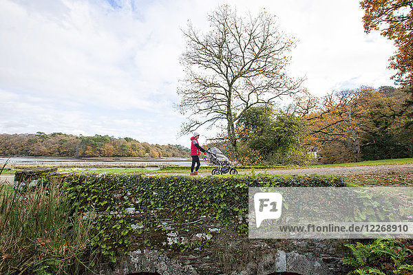 Side view of woman walking with baby carriage on old stone bridge at National Forest of Carnoet during Fall season  Finistere  Brittany  France
