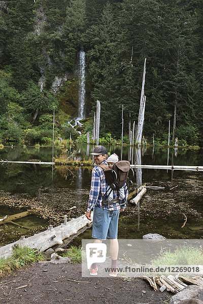 Father standing with baby daughter in front of forest lake  Washington  USA