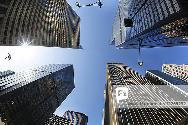 Blick aus niedrigem Winkel von der städtischen Straße auf den klaren Himmel  Glas- und Stahlfassaden hoher Wolkenkratzer und die Ebene am Himmel
