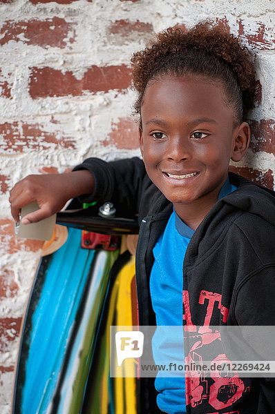 Porträt eines Jungen im Freien  der ein Skateboard hält und lächelt